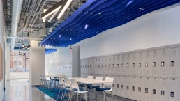 his lounge and study area is enhanced with additional lockers, vibrant blue and gray carpeting, and a felt wave-shaped sound-dampening structure above the table and chairs, creating a comfortable and focused environment.