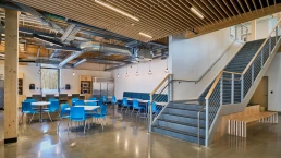 Interior shot of cafe and student lounge of new building. Featuring cross laminated timber, concrete floors, and bright blue accents.