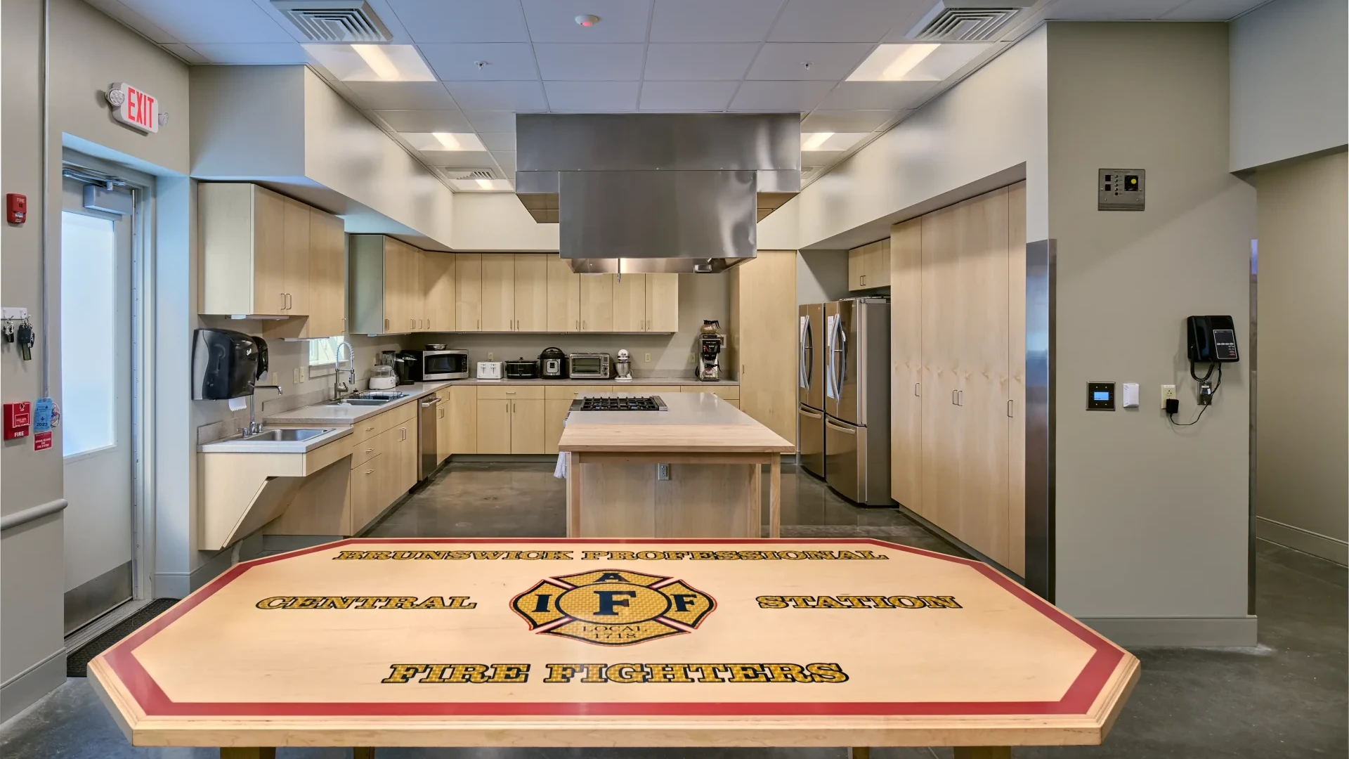 Modern kitchen area inside the Brunswick Fire Station, featuring a large island and fire department-themed table.